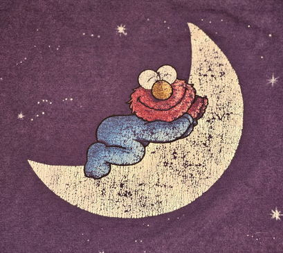 Close-up of the t-shirt print — baby Elmo asleep, curled on a glowing crescent moon among stars.