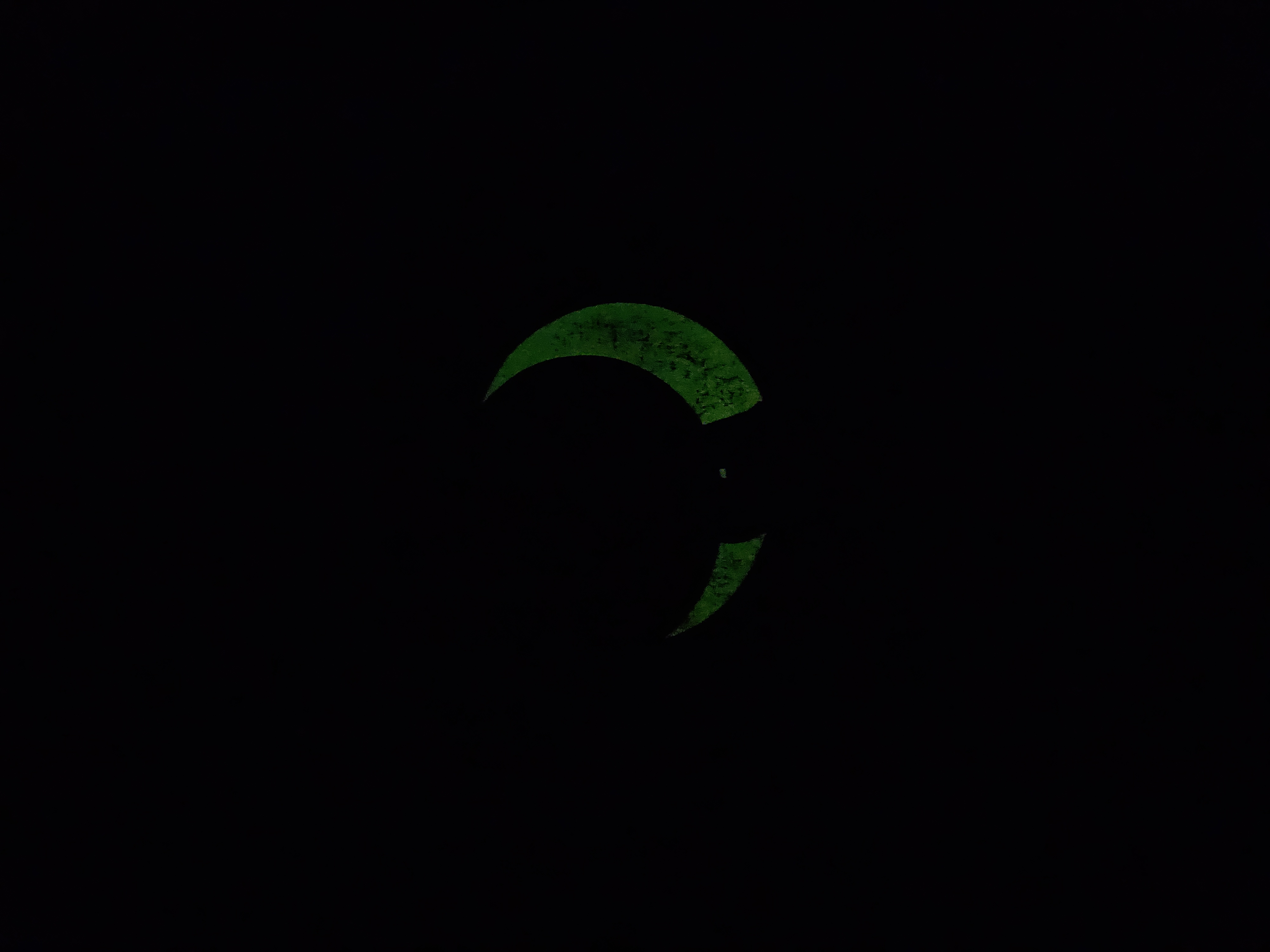 The same t-shirt photographed in the dark — only the crescent moon glows, a soft green against black.