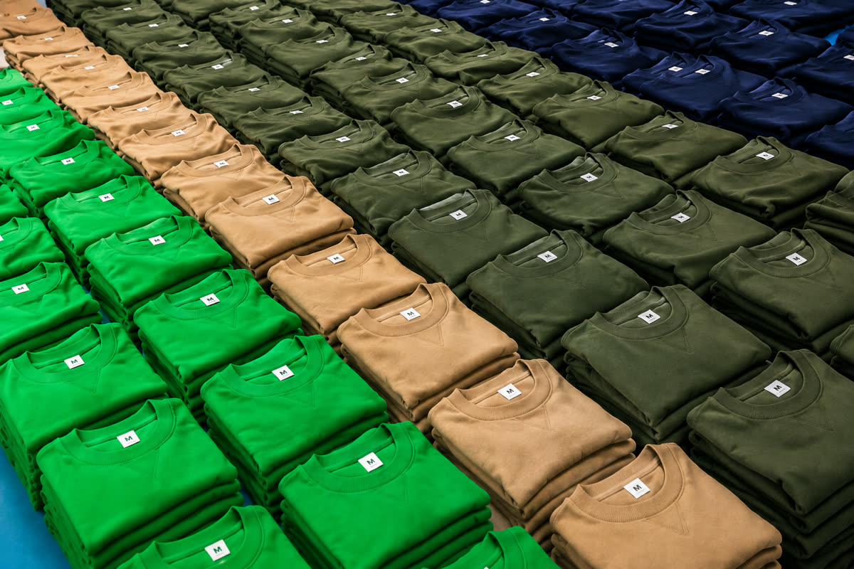 Rows of neatly folded unsold sweatshirts in green, tan, olive and navy, sorted by colour with size tags